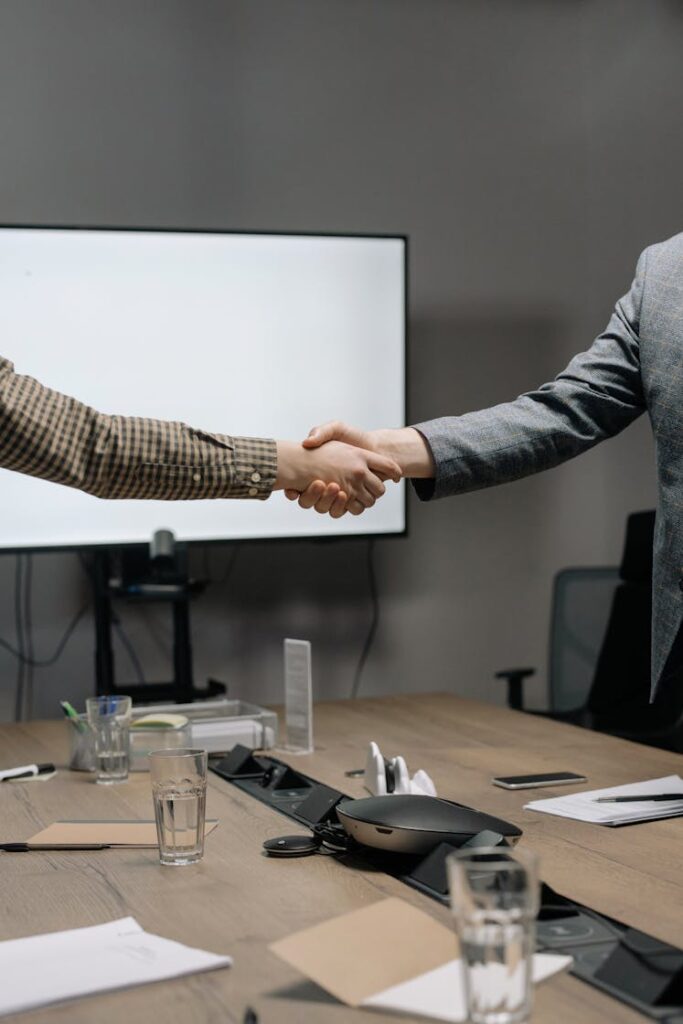 Two executives shaking hands over a business table after an executive coaching session.